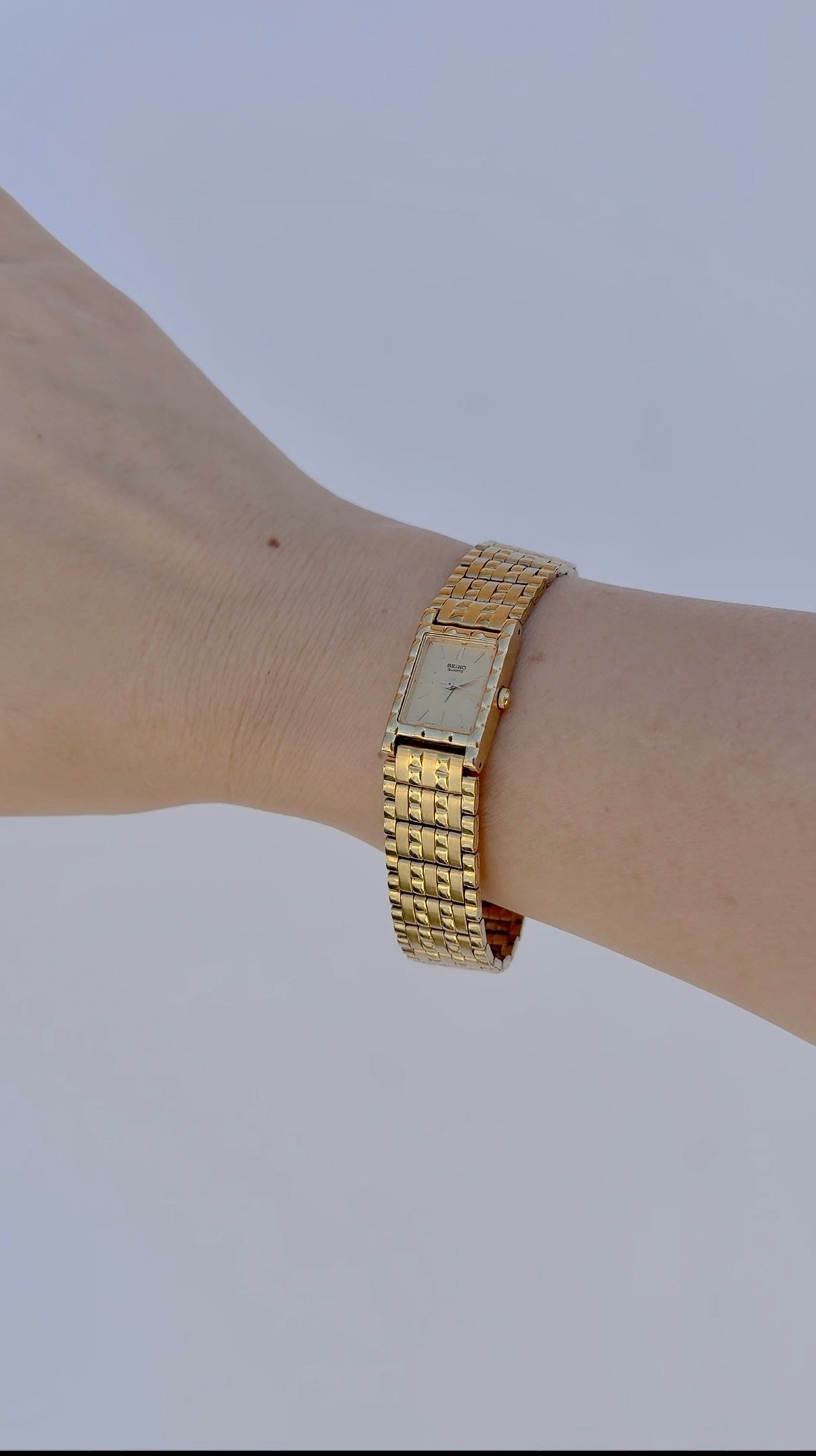 Gold wristwatch on a wrist with a plain background